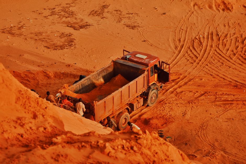A dump truck and workers at a red soil extraction site, highlighting industrial work.