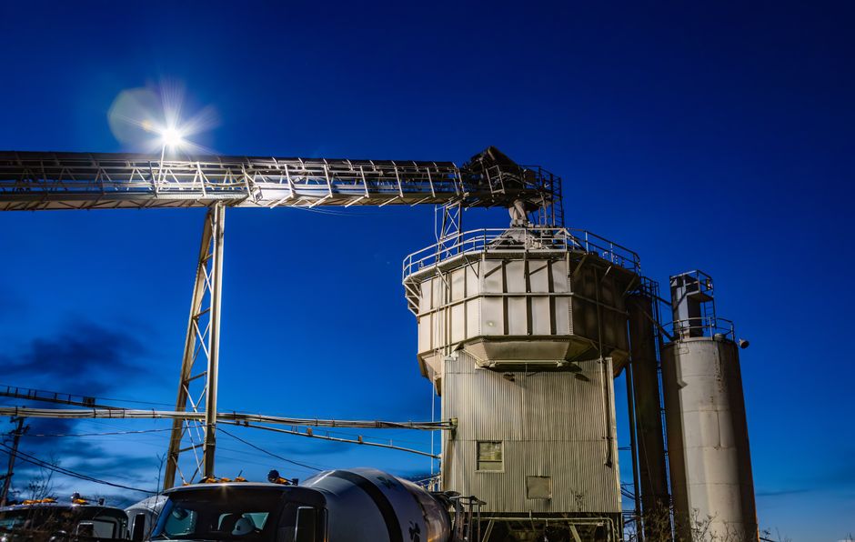 An industrial plant with silos and machinery illuminated at night with a clear sky.