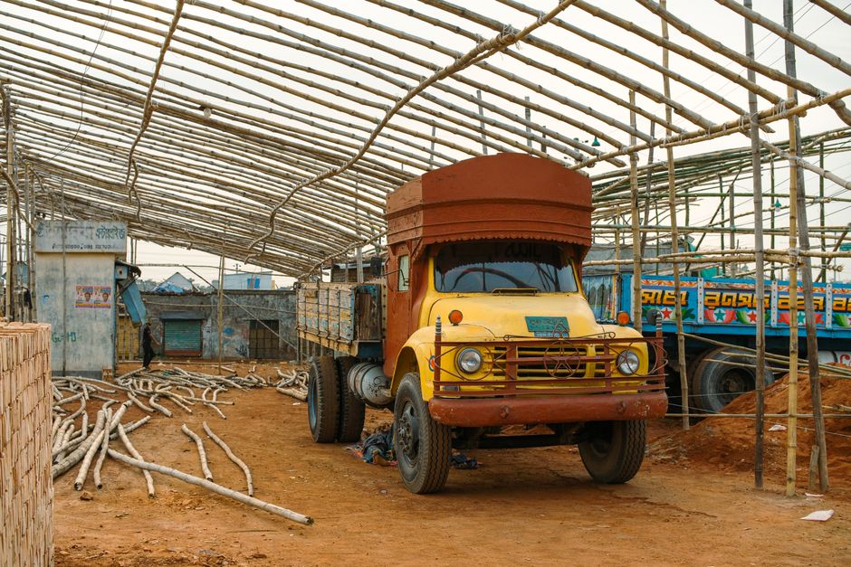 A rustic yellow truck parked inside a partially built bamboo structure, capturing a unique industrial scene.
