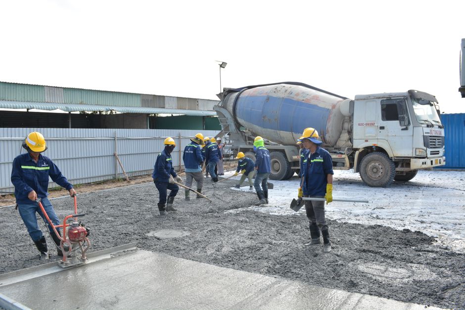 Workers in safety gear pouring concrete outdoors with a cement mixer truck.